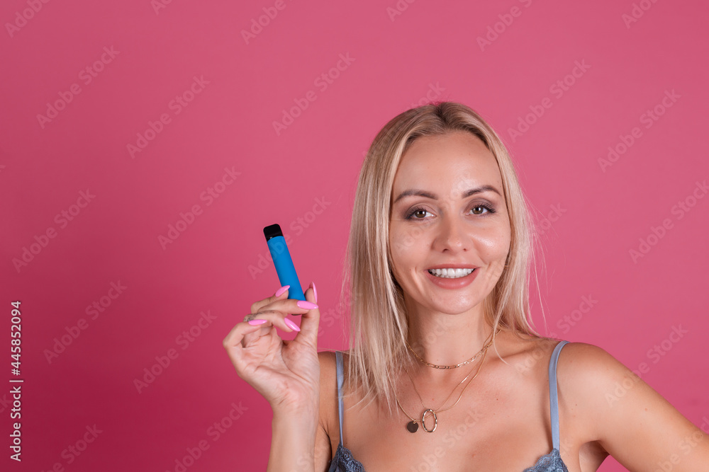 Beautiful blonde woman in silk dress isolated on pink background holding electronic cigarette Beautiful blonde woman in silk dress isolated on pink background holding electronic cigarette