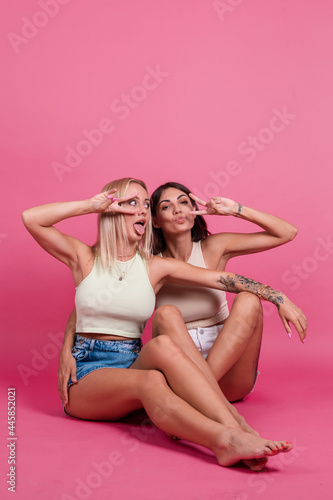 Two girl friends in casual on pink background having fun together, smile and laugh, friendship concept