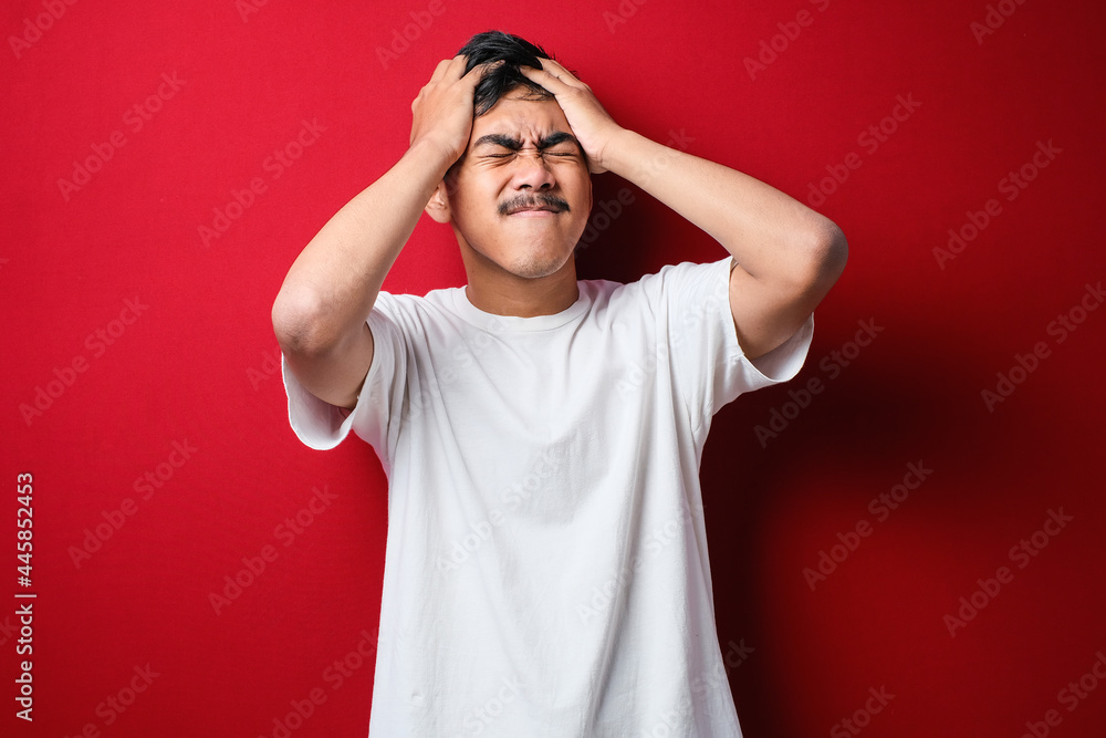 Young handsome asian man wearing white t-shirt with hand on head for pain in head because stress. Suffering migraine. Young handsome asian man wearing white t-shirt with hand on head for pain in head because stress. Suffering migraine.