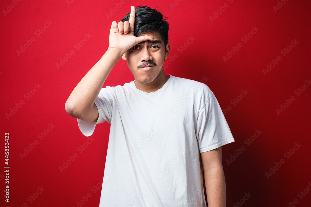 Fototapeta premium Young handsome man wearing white t-shirt making fun of people with fingers on forehead doing loser gesture mocking and insulting.