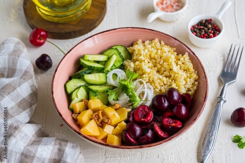 Healthy Salad Bowl with Bulgur, Cherry, Cheese, Cucumber and Walnuts on a light concrete background. Healthy food.