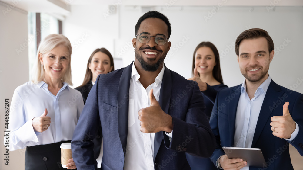 Happy African American business leader and team making thumb up like gesture at camera. Head shot portrait of young millennial businessman, boss standing in front of employees group. Team work concept Happy African American business leader and team making thumb up like gesture at camera. Head shot portrait of young millennial businessman, boss standing in front of employees group. Team work concept