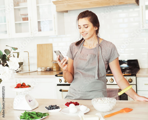 Lifestyle, cooking and freelance concept: young happy woman talking on mobile phone while cooking in a kitchen