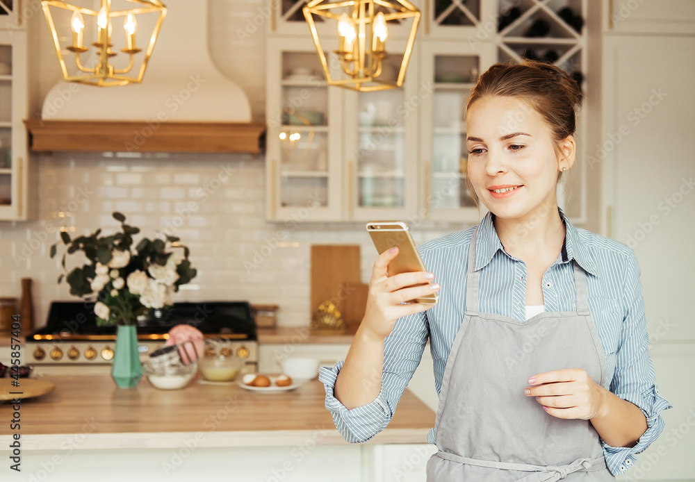 Lifestyle, cooking and freelance concept: young happy woman talking on mobile phone while cooking in a kitchen Lifestyle, cooking and freelance concept: young happy woman talking on mobile phone while cooking in a kitchen
