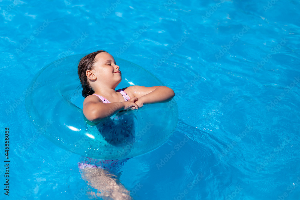 minimalistic trend, blue inflatable swimming circle on the blue water of the pool, a happy girl enjoying the coolness of the water on a hot summer day. 