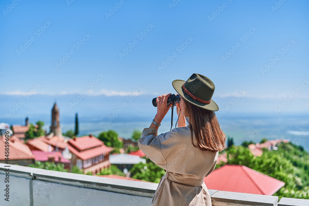 Young girl traveler looks through binoculars during vacation trip on a bright sunny day