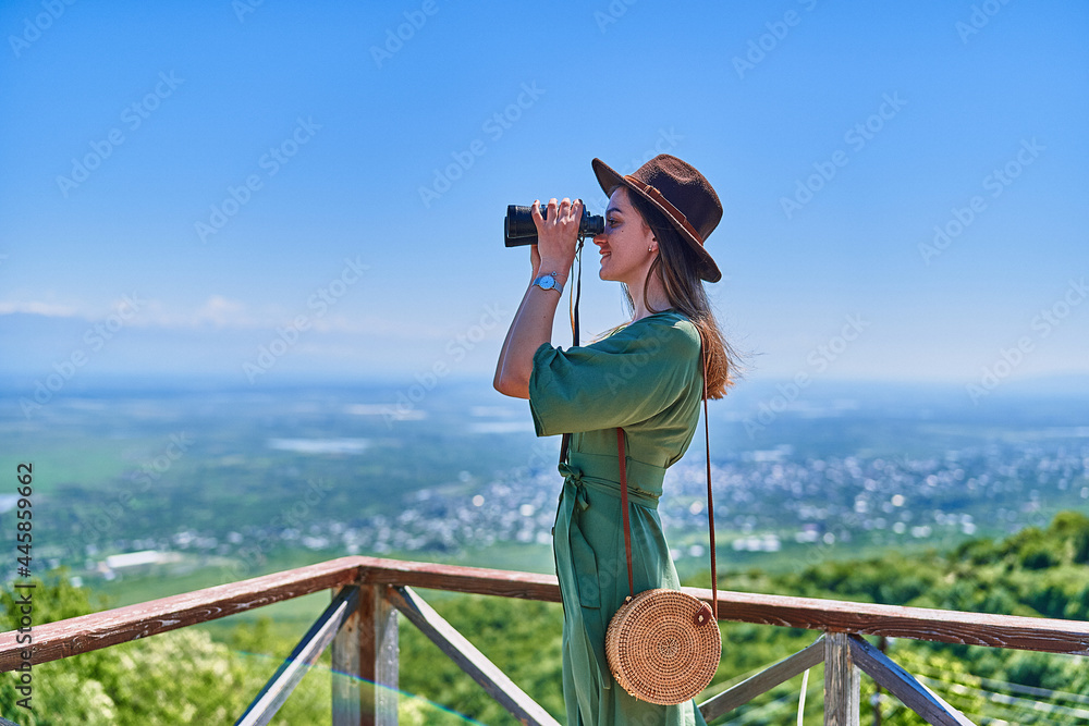 Young girl traveler wearing hat looks through binoculars during vacation weekend trip on a bright sunny day