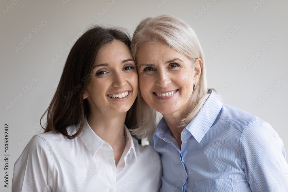 Head shot cheek to cheek portrait of happy senior 60s mother and young grownup daughter. Cute teen millennial granddaughter and beloved grandmother smiling at camera. Intergenerational relations Head shot cheek to cheek portrait of happy senior 60s mother and young grownup daughter. Cute teen millennial granddaughter and beloved grandmother smiling at camera. Intergenerational relations