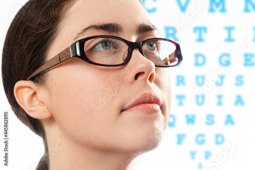 Healthy vision. Close up face of young beautiful woman in glasses looking at a diagram to check her vision. The concept of optical test and ophthalmology