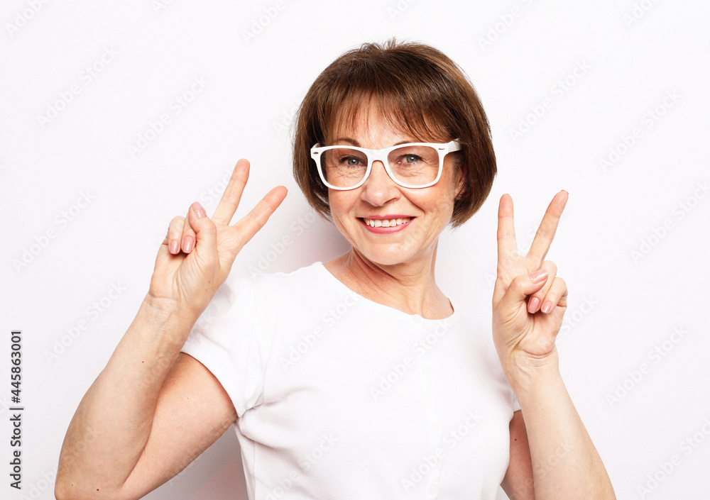 Old people, modern lifestyle, body language concept. Adorable mature wrinkled woman smiles broadly and gives peace sign Old people, modern lifestyle, body language concept. Adorable mature wrinkled woman smiles broadly and gives peace sign