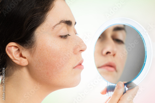 Aesthetic medicine. Profile portrait of a young Caucasian woman looking at her humpback nose in the mirror. The concept of rhinoplasty