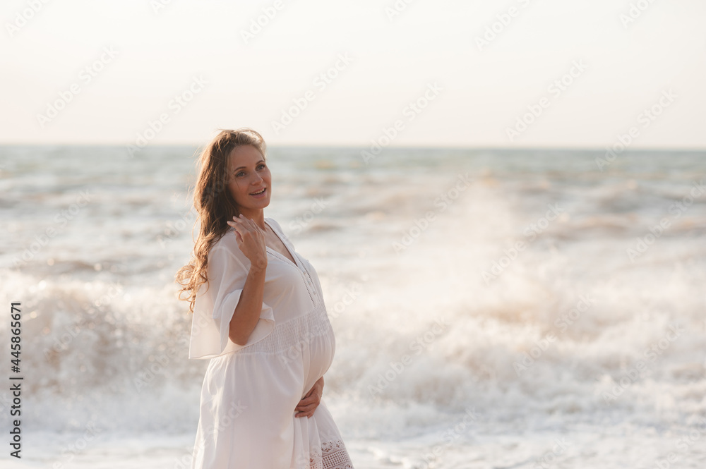 Beautiful laughing pregnant woman wear white dress posing over sea at background closeup. Healthy lifestyle. Motherhood. Maternity. Happiness. Beautiful laughing pregnant woman wear white dress posing over sea at background closeup. Healthy lifestyle. Motherhood. Maternity. Happiness.