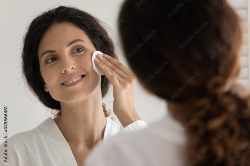 Caring for skin. Pretty millennial hispanic woman do everyday facial skincare procedure cleansing face with cosmetic lotion using cotton sponge. Young female remove makeup at evening by mirror at home Caring for skin. Pretty millennial hispanic woman do everyday facial skincare procedure cleansing face with cosmetic lotion using cotton sponge. Young female remove makeup at evening by mirror at home