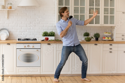 Cooking like a song. Inspired handsome male stand on warm floor barefoot sing aloud distracted of making lunch hold ladle as microphone. Happy young man have fun celebrate renovation at kitchen area