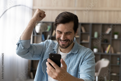 Overjoyed sincere handsome happy young man looking at smartphone screen, celebrating getting amazing unbelievable news, online lottery giveaway win, victory notification, internet success concept. photo