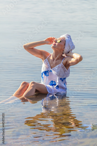 Young woman with cucumbers on her eyes and a towel on her head. Lady sits in the sea .Concept of summer vacation, skin care and health, relaxation, spa