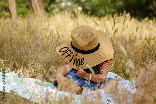 A little infant baby girl in a straw hat in a field. Nature in a summer. Offline