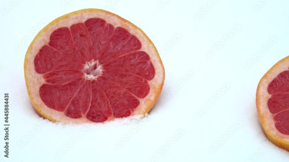 Two halves of cut in half dark red ripe grapefruit lie on white snow