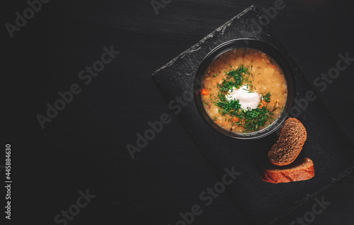 Soup with pickled cucumbers and pearl barley in black bowl on black wooden table background