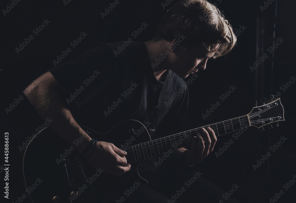Obraz premium Guy in a T-shirt plays an electric guitar on a dark background