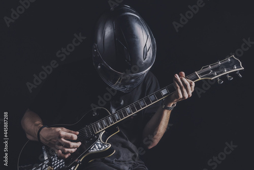 man in motorcycle helmet playing electric guitar on dark background
