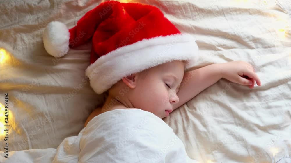 Cute Sleeping Boy in Santa Claus Hat Lying in Bed at Home. Christmas Light. Xmas, New Year Winter Holiday Concept. Dream. Child sleeping before Christmas. Cute Sleeping Boy in Santa Claus Hat Lying in Bed at Home. Christmas Light. Xmas, New Year Winter Holiday Concept. Dream. Child sleeping before Christmas.