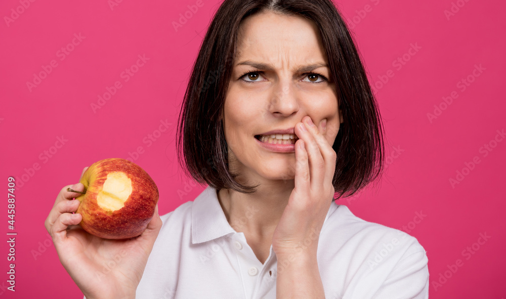 Beautiful young woman bites a big apple and has a toothache Beautiful young woman bites a big apple and has a toothache