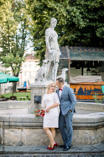 Loving middle-aged couple embracing while leaning backwards on the stone old city fountain and enjoying their date and walk. Beautiful mature couple in old city © sofiko14