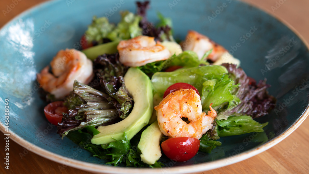 Salad with fresh avocado, lettuce, grilled shrimps, cucumeber on blue dish. Healthy eating. Close up. Selective focus Salad with fresh avocado, lettuce, grilled shrimps, cucumeber on blue dish. Healthy eating. Close up. Selective focus
