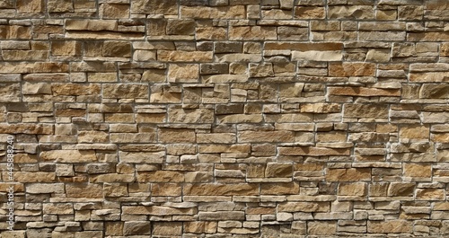 Wall cladding in brown natural stone made from bricks of irregular shape. Background and texture