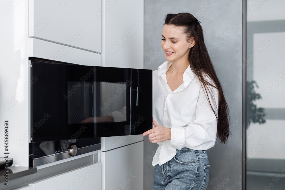 Happy woman opening black microwave door in kitchen Happy woman opening black microwave door in kitchen