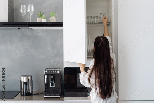 Woman taking cup from shelf in white cupboard