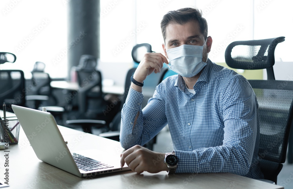 Businessman taking his medical protective mask off while working in the office Businessman taking his medical protective mask off while working in the office