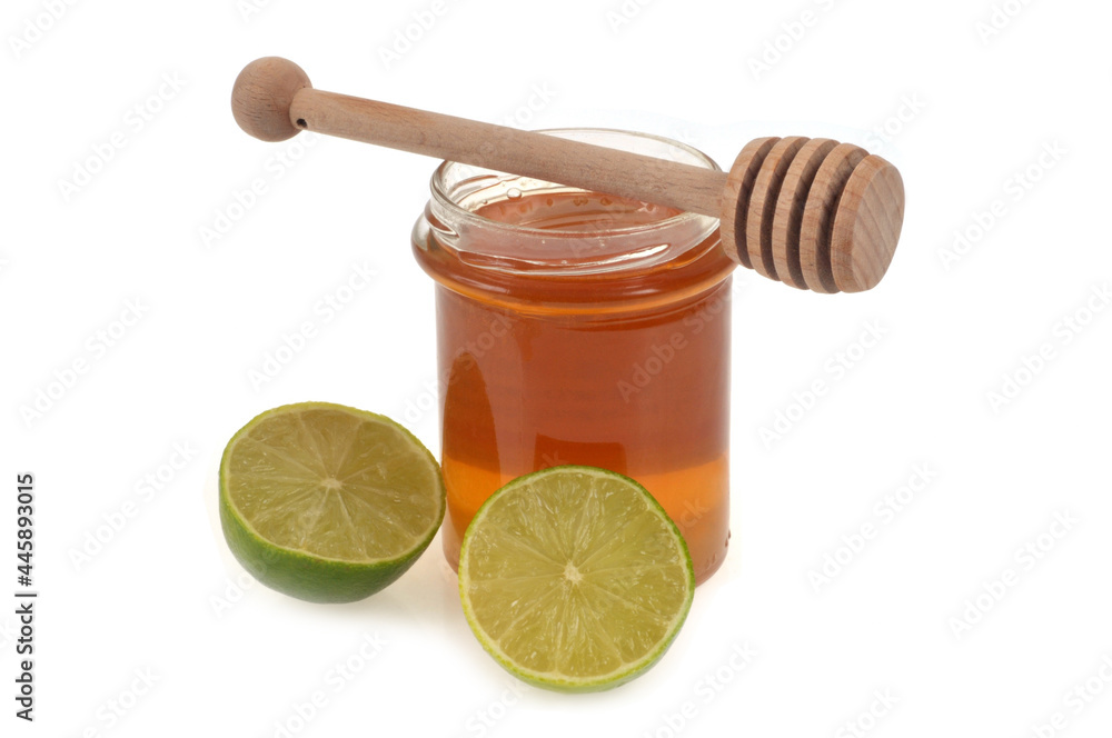 Pot de miel liquide et cuillère à miel à côté d'un citron vert coupé en deux en gros plan sur fond blanc Pot de miel liquide et cuillère à miel à côté d'un citron vert coupé en deux en gros plan sur fond blanc