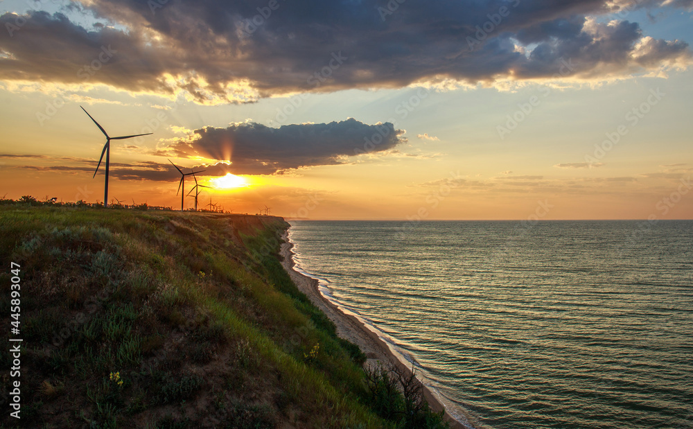 Cliffs over seashore extending to horizon with electricity windmills on background of dramatic sunset sky Cliffs over seashore extending to horizon with electricity windmills on background of dramatic sunset sky