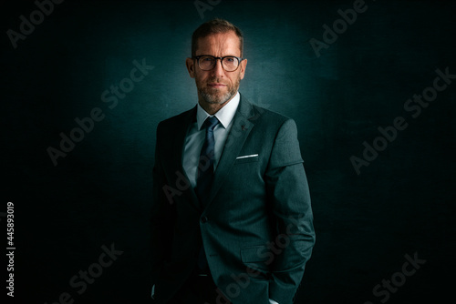 Middle aged businessman wearing suit and tie while standing a isolated dark grey background