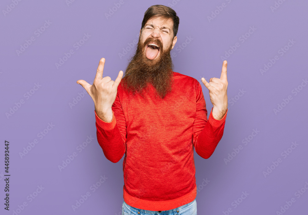 Redhead man with long beard wearing casual clothes shouting with crazy expression doing rock symbol with hands up. music star. heavy concept. Redhead man with long beard wearing casual clothes shouting with crazy expression doing rock symbol with hands up. music star. heavy concept.