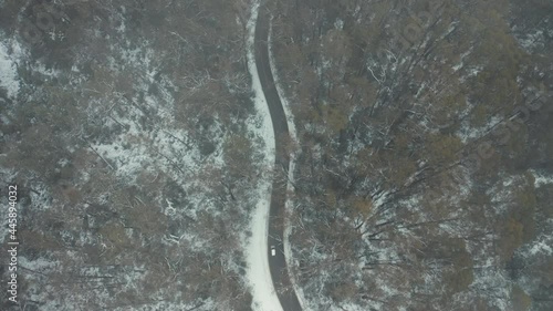 Aerial shot top down cinematic 4k view of white car driving on country road in snow forest at Falls Creek, VIC Australia