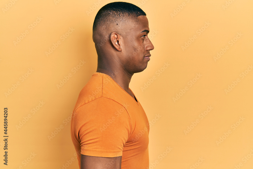 Young black man wearing casual orange t shirt looking to side, relax profile pose with natural face with confident smile. Young black man wearing casual orange t shirt looking to side, relax profile pose with natural face with confident smile.