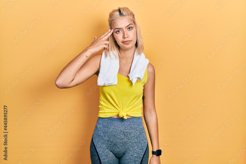 Beautiful blonde sports woman wearing workout outfit shooting and killing oneself pointing hand and fingers to head like gun, suicide gesture. Beautiful blonde sports woman wearing workout outfit shooting and killing oneself pointing hand and fingers to head like gun, suicide gesture.