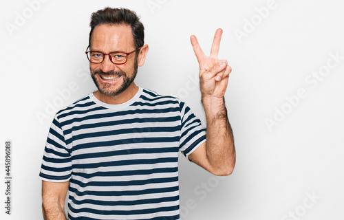 Middle age man wearing casual clothes and glasses smiling with happy face winking at the camera doing victory sign. number two.