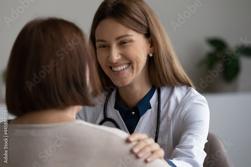 Happy doctor giving support to elder patient, touching shoulder, congratulating on recovery and good medical examination result. Physician talking to retiree with optimistic smile, telling good news