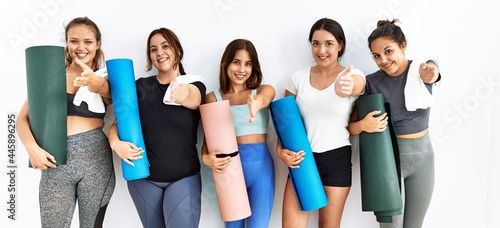 Group of women holding yoga mat standing over isolated background smiling friendly offering handshake as greeting and welcoming. successful business.
