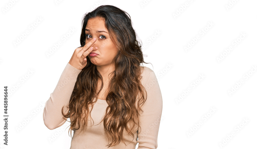 Young hispanic girl wearing casual clothes smelling something stinky and disgusting, intolerable smell, holding breath with fingers on nose. bad smell Young hispanic girl wearing casual clothes smelling something stinky and disgusting, intolerable smell, holding breath with fingers on nose. bad smell