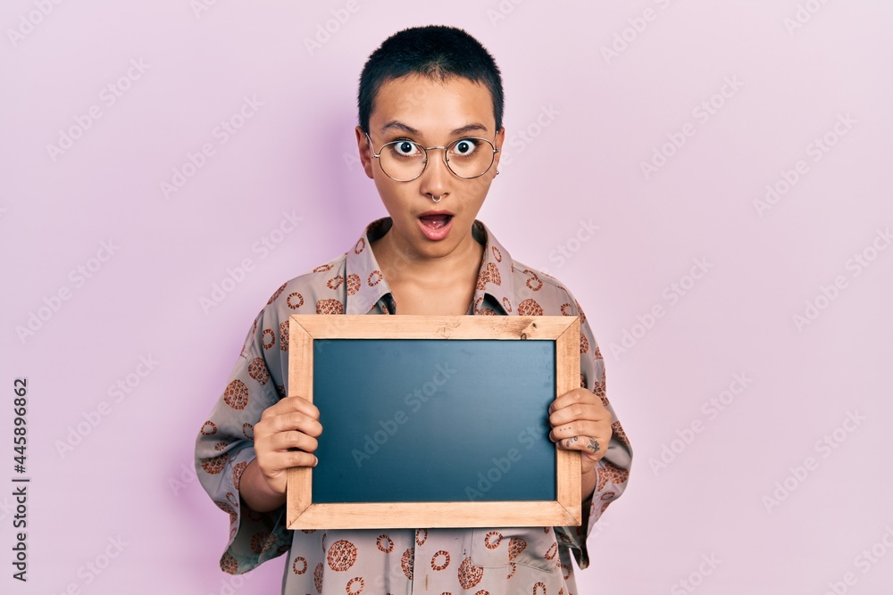 Beautiful hispanic woman with short hair holding blackboard in shock face, looking skeptical and sarcastic, surprised with open mouth Beautiful hispanic woman with short hair holding blackboard in shock face, looking skeptical and sarcastic, surprised with open mouth