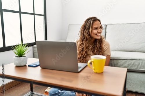 Beautiful hispanic woman using computer laptop at home looking away to side with smile on face, natural expression. laughing confident.