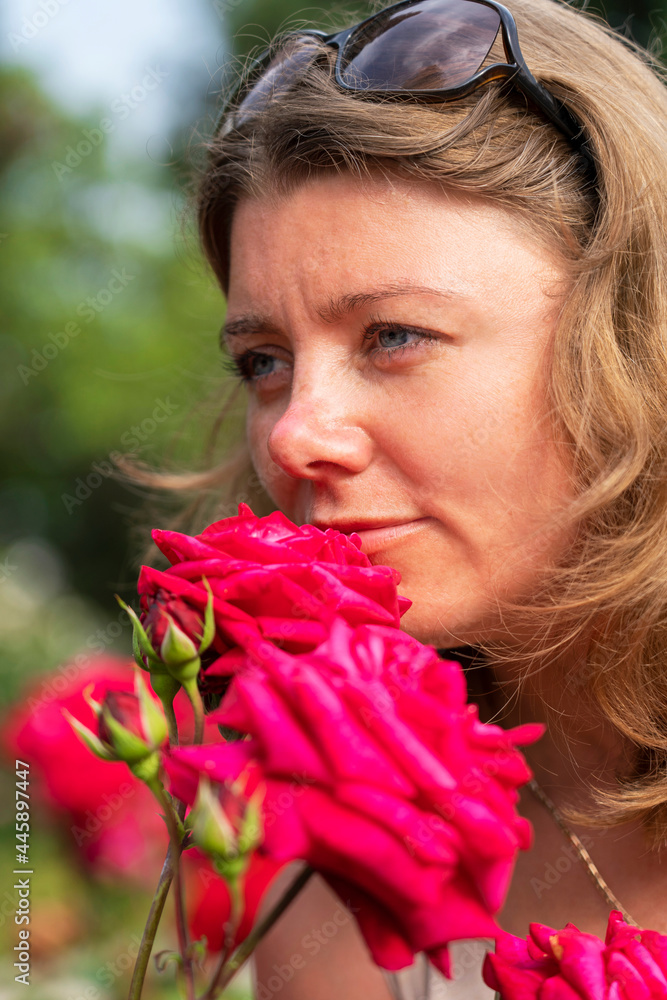 Fototapeta premium Outdoor photo of romantic young woman in rose garden. Smiling woman posing near blooming roses in park.