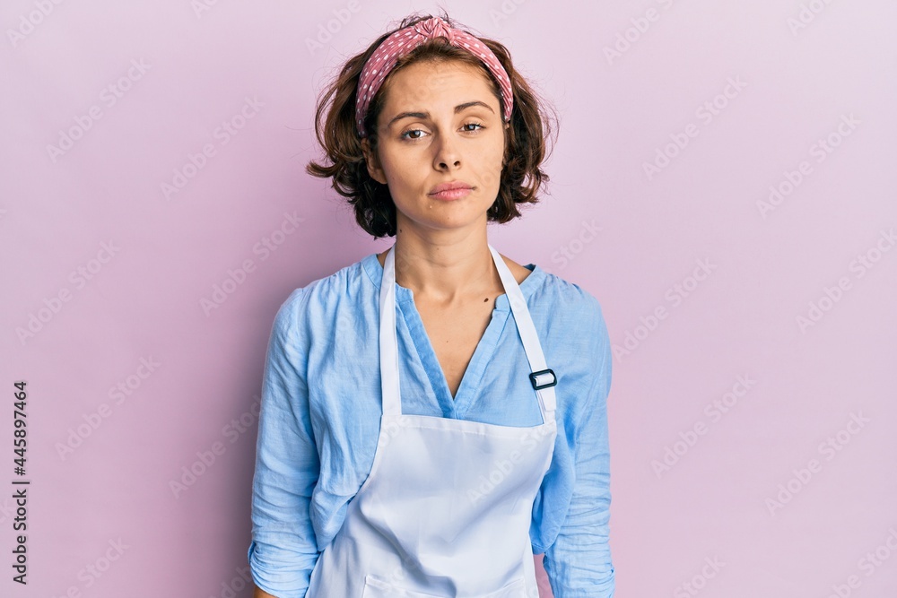 Young brunette woman wearing cleaner apron and gloves with serious expression on face. simple and natural looking at the camera. Young brunette woman wearing cleaner apron and gloves with serious expression on face. simple and natural looking at the camera.