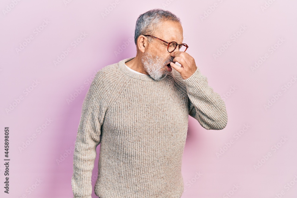 Handsome senior man with beard wearing casual sweater and glasses smelling something stinky and disgusting, intolerable smell, holding breath with fingers on nose. bad smell Handsome senior man with beard wearing casual sweater and glasses smelling something stinky and disgusting, intolerable smell, holding breath with fingers on nose. bad smell