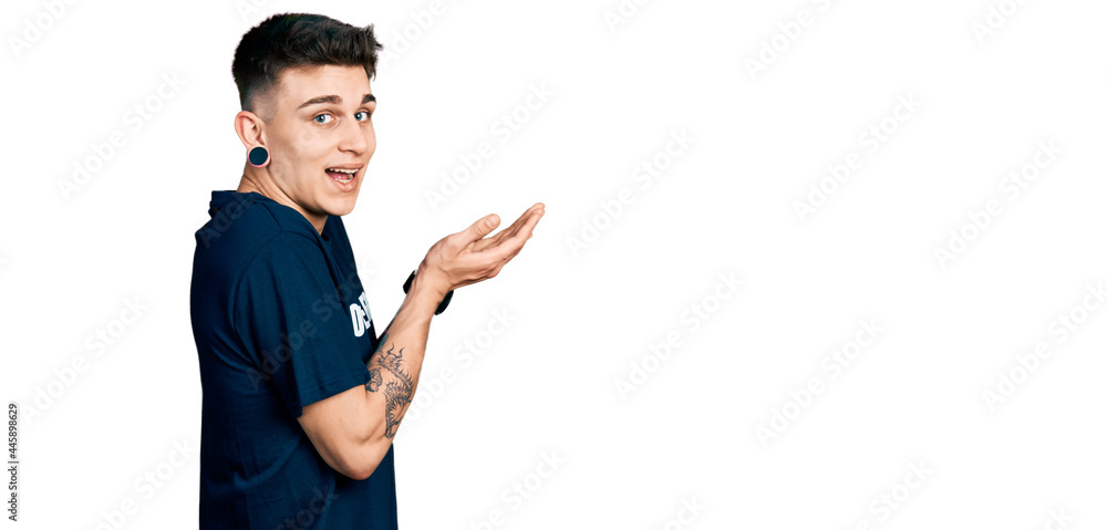 Young caucasian boy with ears dilation wearing volunteer t shirt pointing aside with hands open palms showing copy space, presenting advertisement smiling excited happy Young caucasian boy with ears dilation wearing volunteer t shirt pointing aside with hands open palms showing copy space, presenting advertisement smiling excited happy